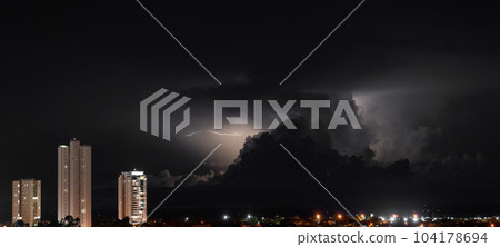 Three Skyscrapers Rise Above the Dark Cityscape During a Stormy Night 104178694