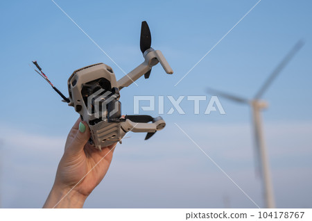 Woman holding a crashed drone against the backdrop of windmills. Woman holding a crashed drone against the backdrop of windmills. 104178767