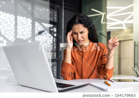 Overworked and tired woman working inside office at workplace, businesswoman using laptop at work, latin american woman having severe headache frustrated with achievement result. Overworked and tired woman working inside office at workplace, businesswoman using laptop at work, latin american woman having severe headache frustrated with achievement result. 104179663