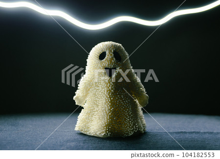 A toy smiling ghost stands in the semi-darkness and a strip of light above it A toy smiling ghost stands in the semi-darkness and a strip of light above it 104182553