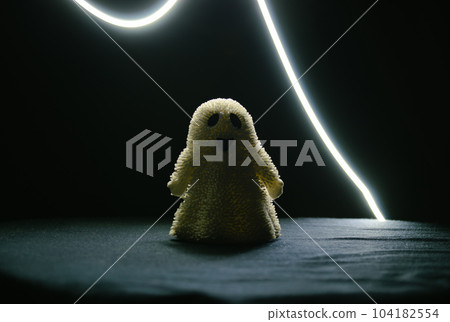 A toy smiling ghost stands in the semi-darkness and a strip of light above it A toy smiling ghost stands in the semi-darkness and a strip of light above it 104182554
