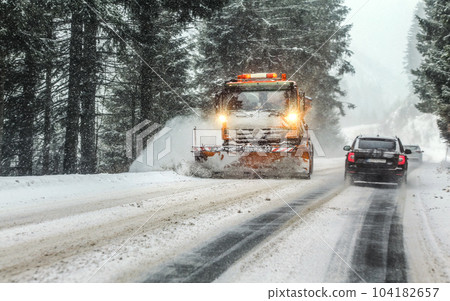 View from car behind forest road through snowstorm blizzard, orange maintenance plough truck coming opposite way, dangerous driving conditions View from car behind forest road through snowstorm blizzard, orange maintenance plough truck coming opposite way, dangerous driving conditions 104182657