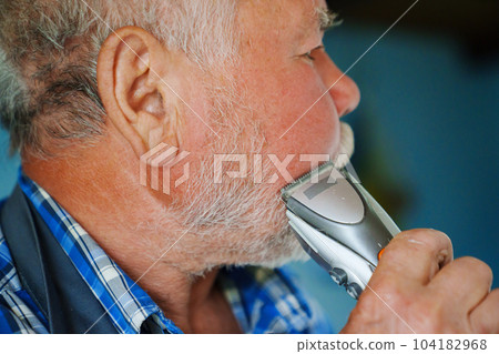 An elderly man trims his beard with an eclectic razor. ease of use of clippers. 104182968