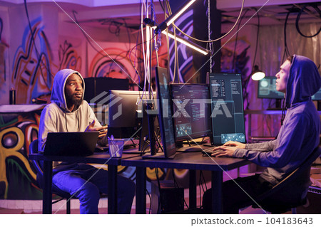 Internet criminals planning cyberattack and malicious software programming. Asian and african american hackers talking about illegal ransomware coding while cracking password on computers Internet criminals planning cyberattack and malicious software programming. Asian and african american hackers talking about illegal ransomware coding while cracking password on computers 104183643