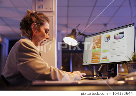 Businesswoman analyzing marketing statistics, working late at night at financial strategy in startup office. Executive manager planning business investment to help increase company profit 104183644