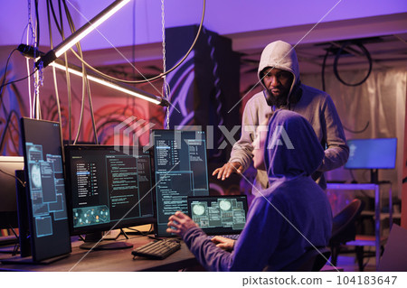 Hackers working together and coding ransomware on multiple computer screens. Internet thieves team planning cyberattack to stealing information from database server in hideout 104183647