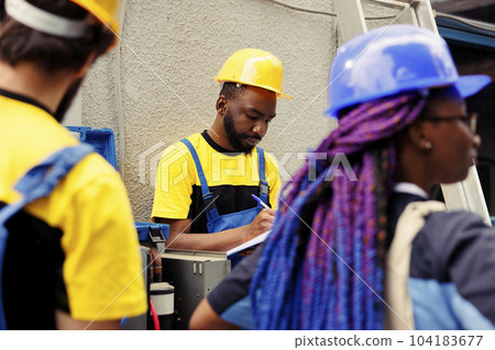 Diverse team of seasoned mechanics brainstorming possible ways to recondition defective outdoor condenser. Adept repairmen commissioned by home owner to patch up broken air conditioner Diverse team of seasoned mechanics brainstorming possible ways to recondition defective outdoor condenser. Adept repairmen commissioned by home owner to patch up broken air conditioner 104183677