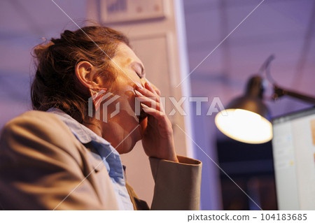 Tired exhausted executive manager yawning in startup office after working overhours at marketing strategy, analyzing financial graphs report. Overworked entrepreneur checking company statistics 104183685