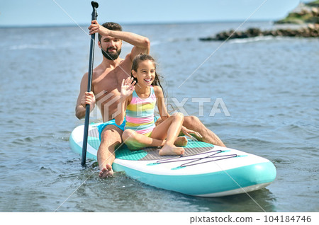 Father and daughter surfing on sup board and having funny time, family summer vacations. 104184746