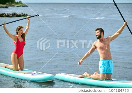Couple of tourists young man and woman having fun paddleboarding at sea, enjoying summer vacation. Couple of tourists young man and woman having fun paddleboarding at sea, enjoying summer vacation. 104184753