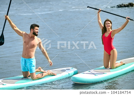 Couple of tourists young man and woman having fun paddleboarding at sea, enjoying summer vacation. Couple of tourists young man and woman having fun paddleboarding at sea, enjoying summer vacation. 104184754