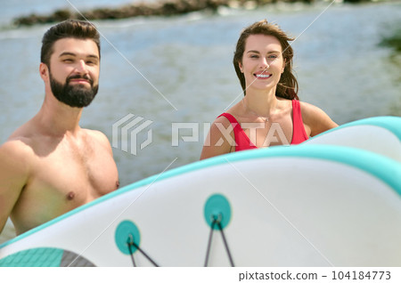 Attractive man and woman young surfers on beach, enjoying vacation near sea and extreme sport. Attractive man and woman young surfers on beach, enjoying vacation near sea and extreme sport. 104184773