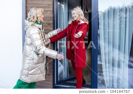 Happy female welcoming her guest outside the house Happy female welcoming her guest outside the house 104184787