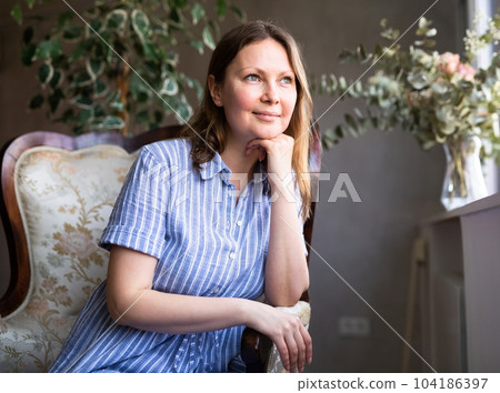 Girl is sitting in semi-dark room among indoor plants of ficus trees and remembers plot of book 104186397