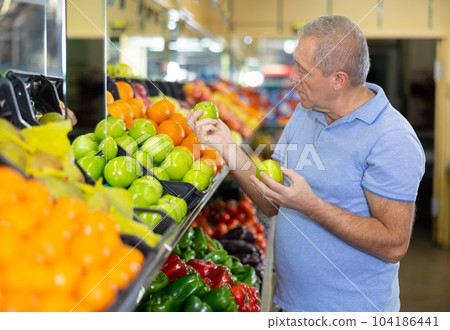 Concentrated mature male buyer pensioner choosing organic granny smith green apples in hypermarket Concentrated mature male buyer pensioner choosing organic granny smith green apples in hypermarket 104186441