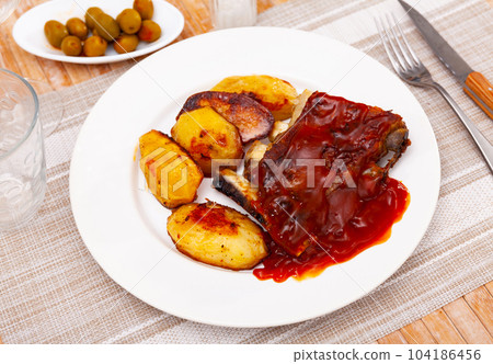 Portion of roasted pork ribs with pieces of fried potatoes 104186456
