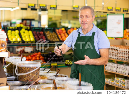 Elderly salesman showing olives in grocery store Elderly salesman showing olives in grocery store 104186472