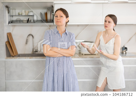 Offended mother standing in the kitchen, upset young daughter talking 104186712