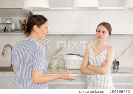 Kind middle-aged mother talking to young daughter in the kitchen Kind middle-aged mother talking to young daughter in the kitchen 104186770