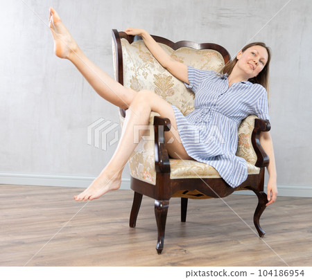 Girl settled down in vintage armchair with legs raised on armrest , put feet on handle of furniture Girl settled down in vintage armchair with legs raised on armrest , put feet on handle of furniture 104186954