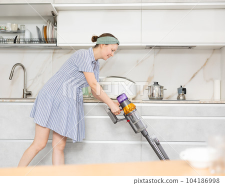 Housewife using vacuum cleaner removes dust in room Housewife using vacuum cleaner removes dust in room 104186998