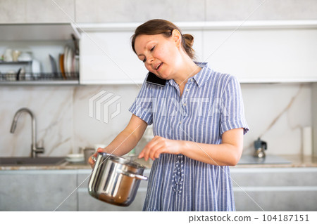 Inexperienced housewife holds saucepan in hands and calls asking for cooking advice Inexperienced housewife holds saucepan in hands and calls asking for cooking advice 104187151