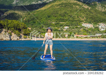 Young women Having Fun Stand Up Paddling in blue water sea near st stefan island in Montenegro. SUP Young women Having Fun Stand Up Paddling in blue water sea near st stefan island in Montenegro. SUP 104189262