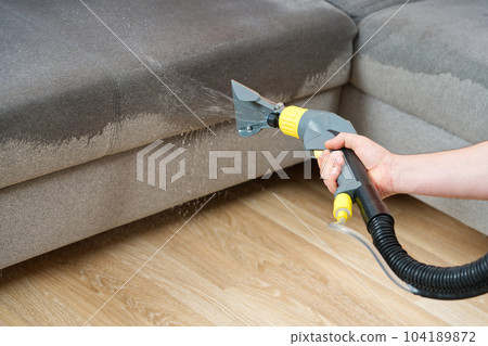 Dry cleaner's man employee removing dirt from textile furniture in flat. closeup, vacuum clean sofa Dry cleaner's man employee removing dirt from textile furniture in flat. closeup, vacuum clean sofa 104189872
