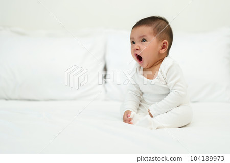 infant baby sitting and yawning on bed 104189973
