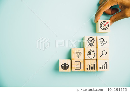 Hand arranging wood block stacking to depict the business strategy and action plan on blue background. Showcasing the concept of business development and targeting business goals. Copy space included Hand arranging wood block stacking to depict the business strategy and action plan on blue background. Showcasing the concept of business development and targeting business goals. Copy space included 104191353