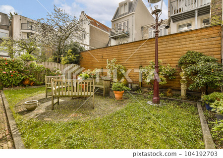 a backyard with lots of plants and flowers on the lawn, including an old wooden bench in the middle part of the yard 104192703