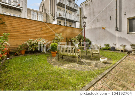 a backyard area with a bench, chair and potted planter on the ground in front of an apartment building a backyard area with a bench, chair and potted planter on the ground in front of an apartment building 104192704