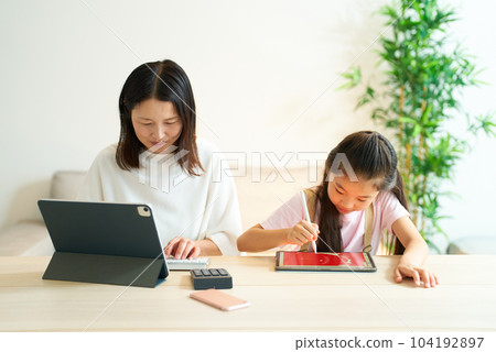 一個女孩和一個使用平板電腦工作的女人玩耍 一個女孩和一個使用平板電腦工作的女人玩耍 104192897