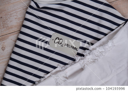 CO2 neutral emission text note on stack of clothes. Ecology nature friendly, climate change, green fuel and earth protect concept. Carbon emission paper recycled label. Natural organic jeans clothing 104193996