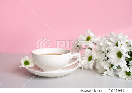 White set cup with plate stand on a pink background with white chamomile flowers White set cup with plate stand on a pink background with white chamomile flowers 104194144