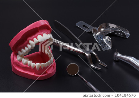 Stainless steel dental tools and layout of a human jaw on the black background. 104194570