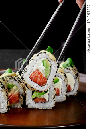 One Philadelphia roll in sesame with salmon grasped from plate by chopsticks 104195362