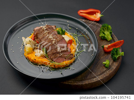 A deliciously appetizing pumpkin puree with chunks of beef meat with spices and herbs in a green plate on a dark table. A hearty lunch in a restaurant. Meat with vegetables in the oven 104195741