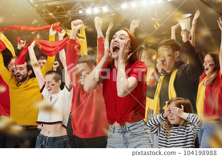 Young people, football fans attending match to watch game and loudly cheering up favourite sport team. Little girl, child closing her eyes Young people, football fans attending match to watch game and loudly cheering up favourite sport team. Little girl, child closing her eyes 104198988