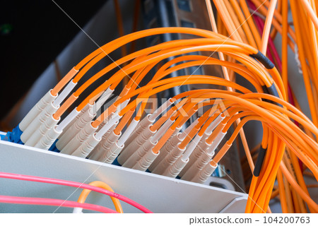 fiber optic cables plugged in network switch panel inside data center 104200763