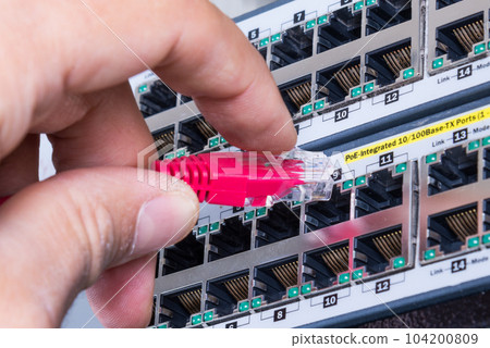 hand of administrator plugging in red patch cable into empty switchboard 104200809