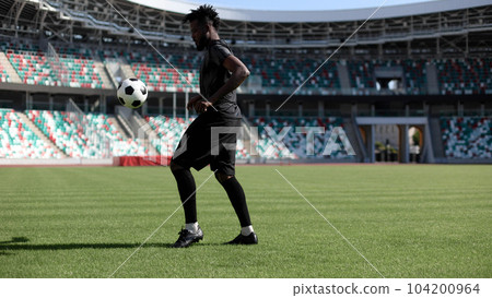 African American man playing football on the stadium field. A man runs with a soccer ball across the field. African American man playing football on the stadium field. A man runs with a soccer ball across the field. 104200964