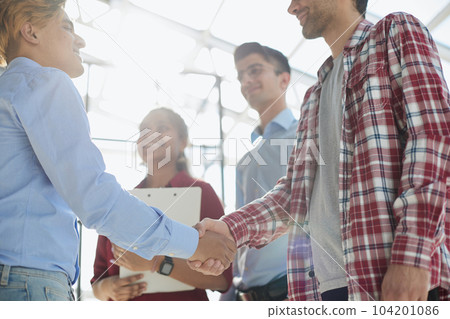 Young startup in casual clothes shaking hands in a modern office space by the window. Young startup in casual clothes shaking hands in a modern office space by the window. 104201086