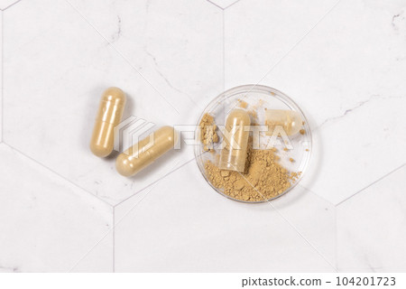 Taking dietary supplements with capsules. One capsule Opened in a jar on marble table Taking dietary supplements with capsules. One capsule Opened in a jar on marble table 104201723