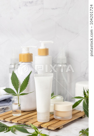 White blank cream tube near green cannabis leaves close up, CBD cosmetic mockup White blank cream tube near green cannabis leaves close up, CBD cosmetic mockup 104201724