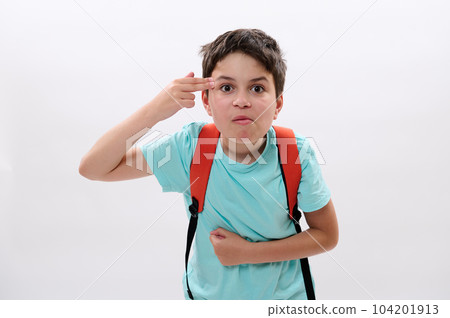 Preteen schoolboy pointing two fingers at his temple, showing a shooting gun hand gesture, feeling stress, suffering for act of bullying, education and puberty problems at school, white background 104201913