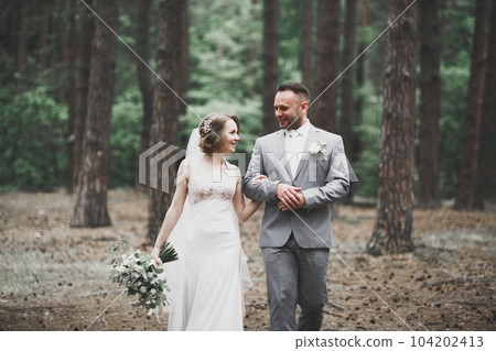 Stylish couple of happy newlyweds walking in the park on their wedding day with bouquet 104202413