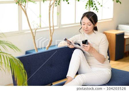 A middle-aged woman looking at a pamphlet with a smartphone in one hand 104203526