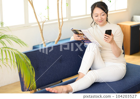 A middle-aged woman looking at a pamphlet with a smartphone in one hand 104203527