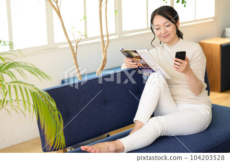 A middle-aged woman looking at a pamphlet with a smartphone in one hand A middle-aged woman looking at a pamphlet with a smartphone in one hand 104203528